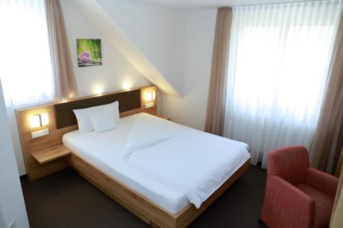 1 dormitorio con 1 cama blanca y 1 silla roja en Hotel Gasthof Schützen, en Laupheim