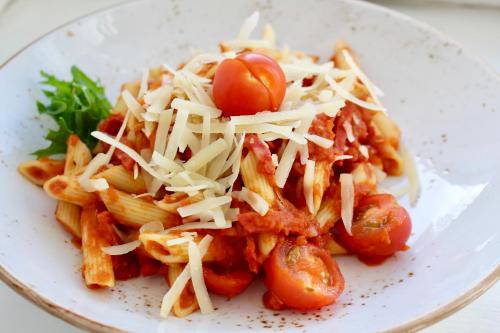 a white plate of pasta with tomatoes and cheese at Rohuaia Apartments in Rakvere