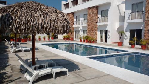 a swimming pool with a straw umbrella and chairs next to a hotel at La Mansi&oacute;n del Faro in Tecolutla