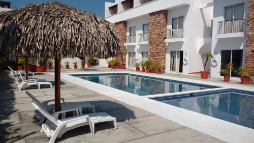 a swimming pool with a straw umbrella and chairs next to a hotel at La Mansión del Faro in Tecolutla