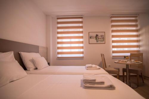 a white bedroom with two beds and a table at Apartmani MG in Trebinje