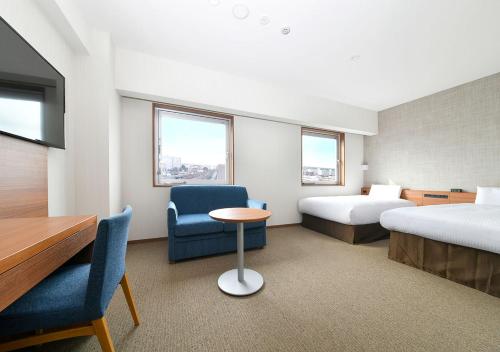 Cette chambre comprend deux lits, une table et une chaise. dans l'établissement JR Inn Chitose, à Chitose