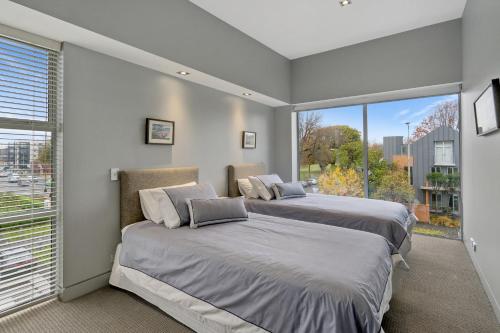 two beds in a room with a large window at City Sanctuary on Kilmore in Christchurch