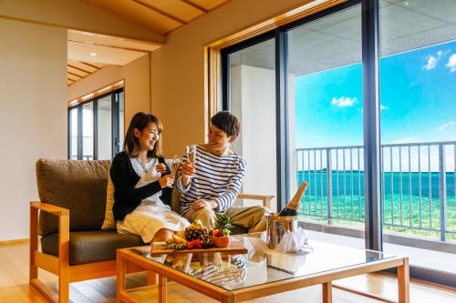 two people sitting on a couch in a living room with a table at Umino Ryotei Okinawa Nakamasou in Onna