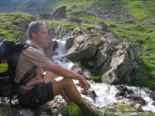 a man with a backpack sitting next to a waterfall at Hotel Montana in Sankt Anton am Arlberg