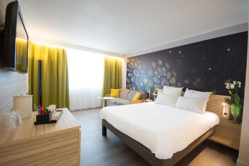 a bedroom with a large white bed and a couch at Novotel Chartres in Chartres