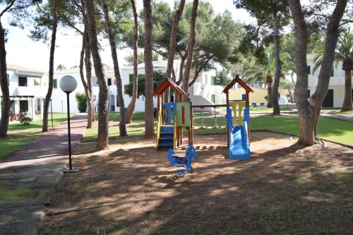 a playground with a slide in a park with trees at Apartamentos Las Brisas I & II in Cala'n Bosch