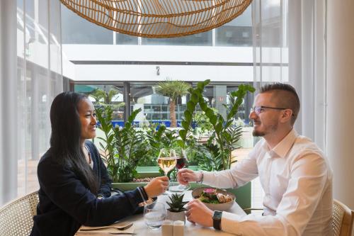 a man and woman sitting at a table with a glass of wine at Novotel Paris Charles de Gaulle Airport in Roissy-en-France