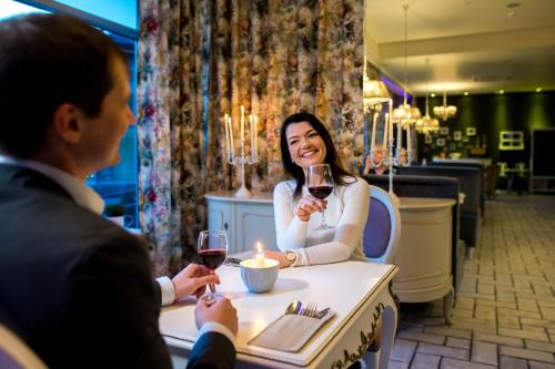a man and woman sitting at a table with wine glasses at Atostogų Parkas Hotel in Palanga