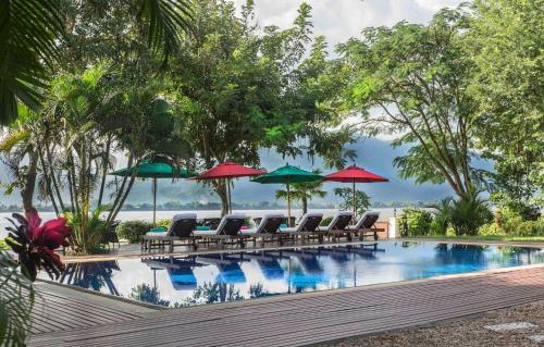 una piscina con tumbonas y sombrillas en La Folie Lodge, en Champasak