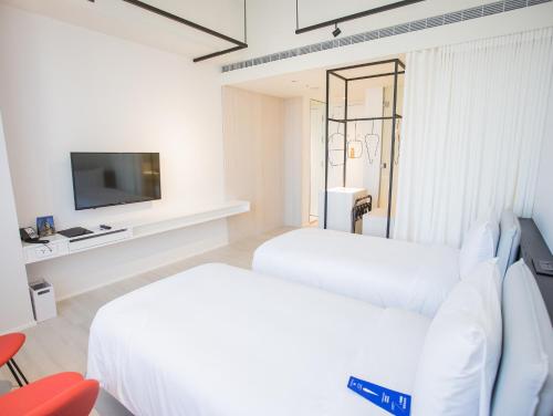 two beds in a white room with a tv at The Place Taichung in Taichung