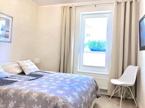 ein Schlafzimmer mit einem Bett, einem Fenster und einem Stuhl in der Unterkunft Apartament Amber Baltic - Rezydencja Ustronie Morskie in Ustronie Morskie