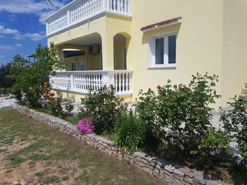 a yellow house with a white balcony and some flowers at Apartmani Marijana in Lozovac