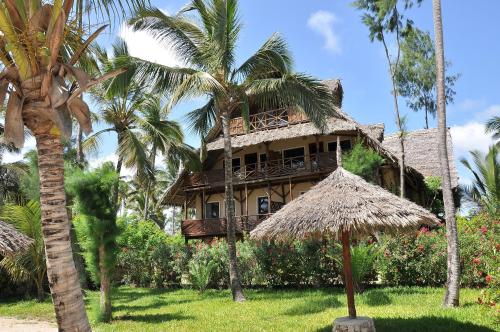 atropical house with a straw roof and palm trees at Palumboreef Beach Resort in Uroa