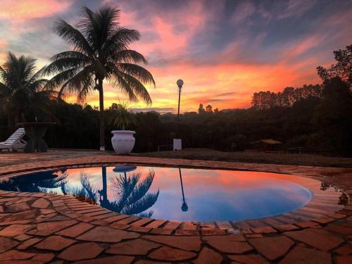 einen Pool mit einer Palme und einem Sonnenuntergang im Hintergrund in der Unterkunft Hotel Paraíso Dos Alpes in São Pedro