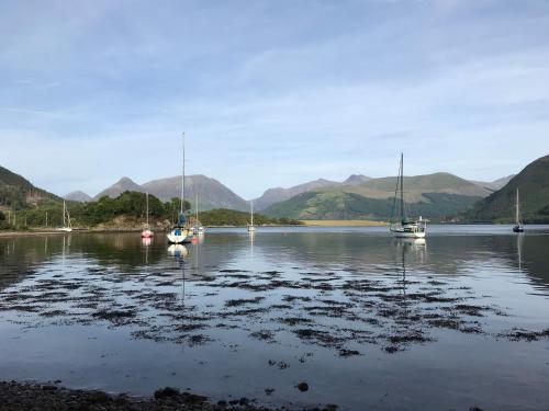 three boats sitting in the water with mountains in the background at The Woolly Rock in North Ballachulish