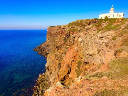 a lighthouse on top of a cliff next to the ocean at West Sardinia Apartments in Càbras