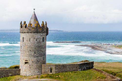 a castle on a hill next to the ocean at Boherbui Cottage on the Wild Atlantic Way in Doolin