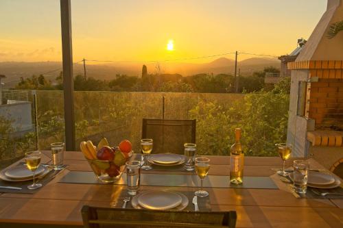 a table with plates and wine glasses and a sunset at Vista Blu Villa in Vlachata