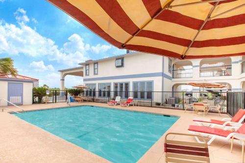 a swimming pool with an umbrella and chairs and a house at Days Inn & Suites by Wyndham Braunig Lake in Elmendorf