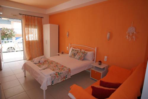 アスプロヴァルタにあるAlexandros Studiosのオレンジ色の壁のベッドルーム1室、ベッド1台、ソファが備わります。