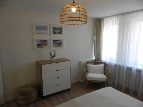 a bedroom with a dresser and a chair and a chandelier at Apartamenty Starówka in Kołobrzeg