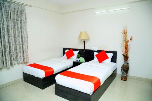 two beds in a hotel room with red and white pillows at Orange Corner, Near Kempegowda Airport, Airport Pickup And Drop Available 24x7 in Bengaluru