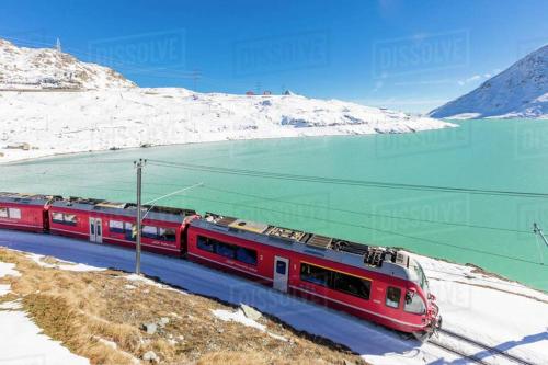 a red train on tracks next to a snow covered mountain at Albergo Motel Dosdè B&B in Grosio