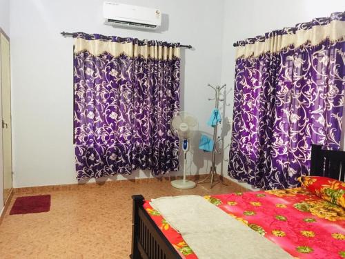 a bedroom with purple curtains and a bed and a fan at 7TH HEAVEN Kannur in Chakkarakkal