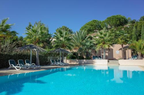 une piscine avec chaises longues, parasols et palmiers dans l'établissement Résidence Stella di Mare, à Sainte-Lucie de Porto-Vecchio