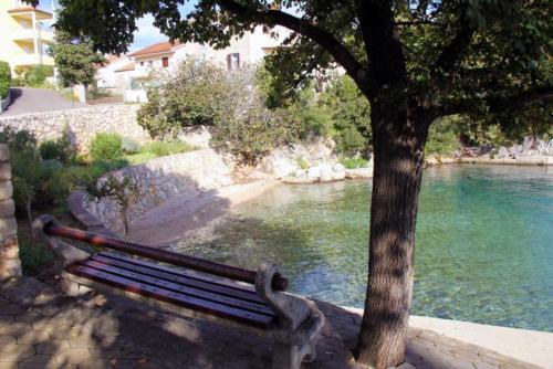 a bench next to a tree next to a river at Apartman Helen in Malinska
