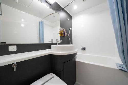 een badkamer met een wastafel, een bad en een spiegel bij Hotel Binario Umeda in Osaka