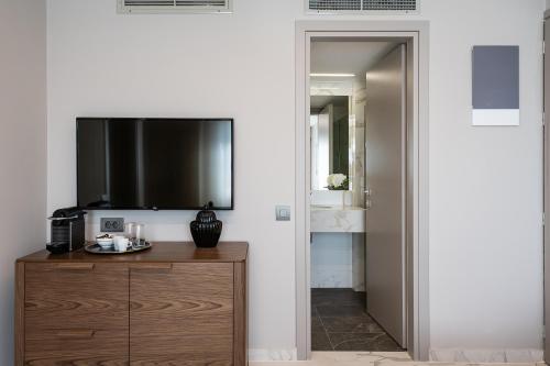 a room with a tv on a wall with a wooden cabinet at Porto Platanias Beach Luxury Selection - Adults Only in Plataniás