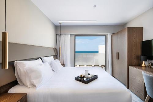 a bedroom with a large white bed and a window at Porto Platanias Beach Luxury Selection - Adults Only in Plataniás