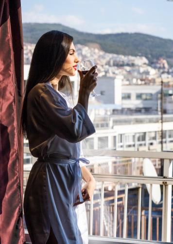 a woman standing on a balcony drinking a wine glass at Vergina Hotel in Thessaloniki