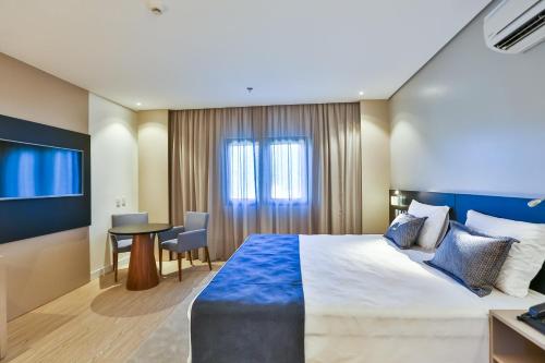 a hotel room with a large bed and a table at Quality Hotel Blumenau in Blumenau