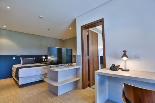 a bedroom with a bed and a desk with a television at Quality Hotel Blumenau in Blumenau