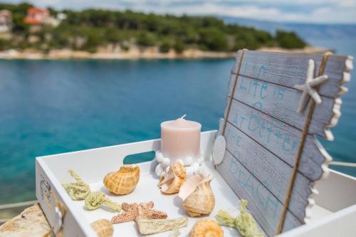 a candle and seashells on a table near the water at Apartments Habek in Vrboska