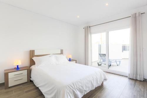 a white bedroom with a bed and a large window at Vitamin Sea, The Terrace Apartment in Baleal