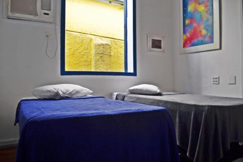 two beds in a room with blue sheets and a window at Brasileranza Hostel in Niterói