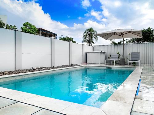 a swimming pool with an umbrella and chairs and a fence at Lamour Holiday Beach House in Gold Coast