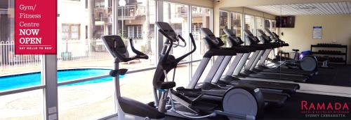 a gym with a row of treadmills next to a swimming pool at Ramada Hotel & Suites by Wyndham Cabramatta in Cabramatta