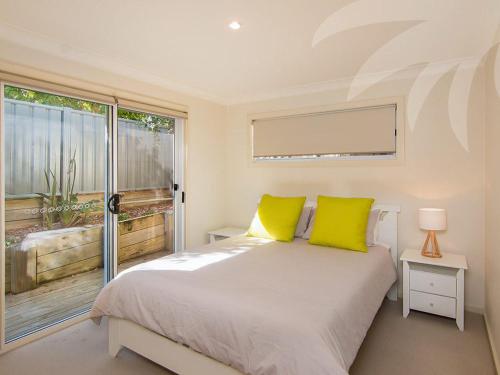 a bedroom with a bed with yellow pillows and a window at Dunes in Blueys Beach