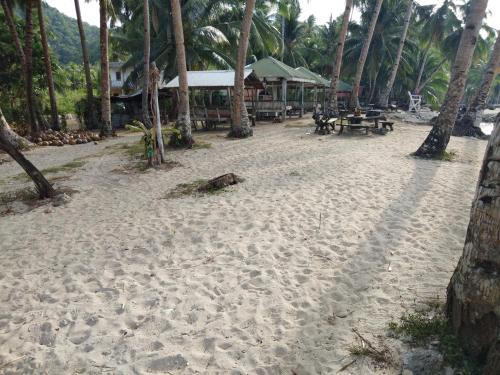 a sandy beach with tables and palm trees at RSK Beach and Accommodation in Dapa