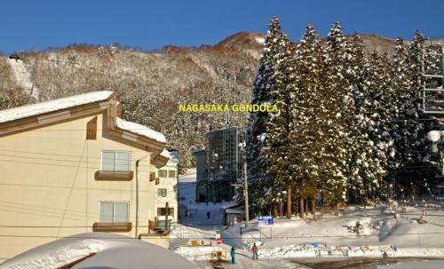 a building with snow on the ground next to trees at Schanze Nozawa in Nozawa Onsen
