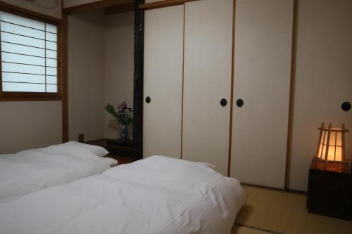 two beds in a bedroom with white cabinets and a window at Stay Omihachiman Ekimae Inn in Omihachiman