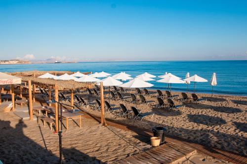 a beach with white umbrellas and chairs and the ocean at Sunny Beach Apartments in Rethymno Town