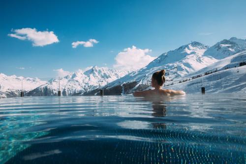 a woman in a infinity pool with snow covered mountains at Hotel Enzian Hochsölden Superior in Sölden