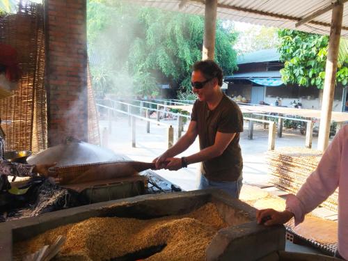 Um homem está a cozinhar comida numa grelha. em Mekong Farmstay CanTho - C.R Floating Market em Can Tho