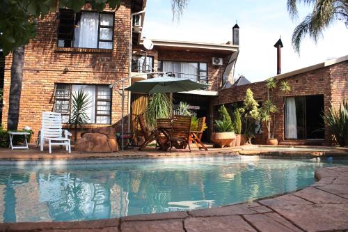 a swimming pool in front of a house with an umbrella at Francor Guesthouse in Pretoria